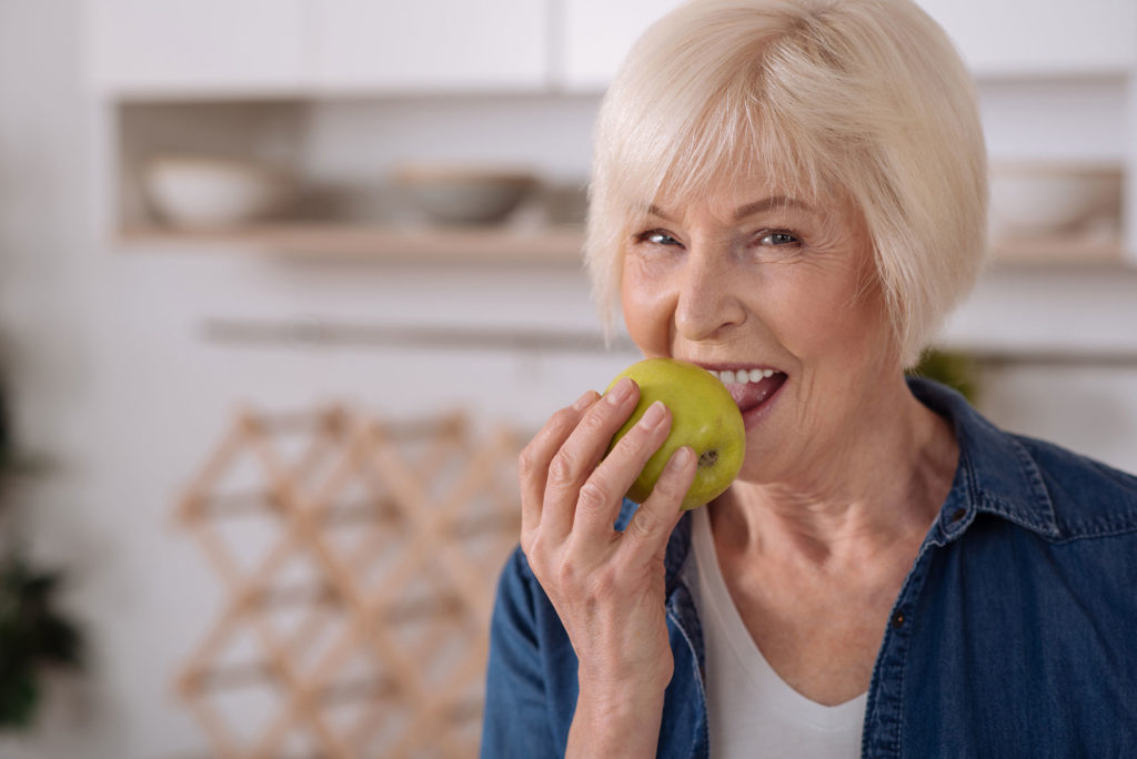 Woman eating apple with implant supported dentures Lexington Park Dentistry Logo Lexington Park, Maryland